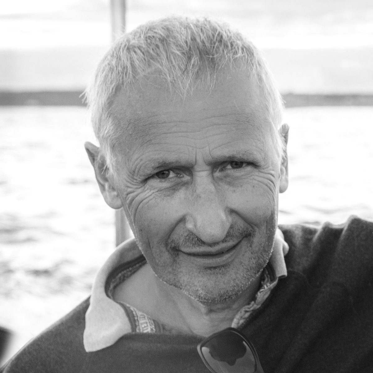 Black and white portrait of James Hodson, smiling, on the water.